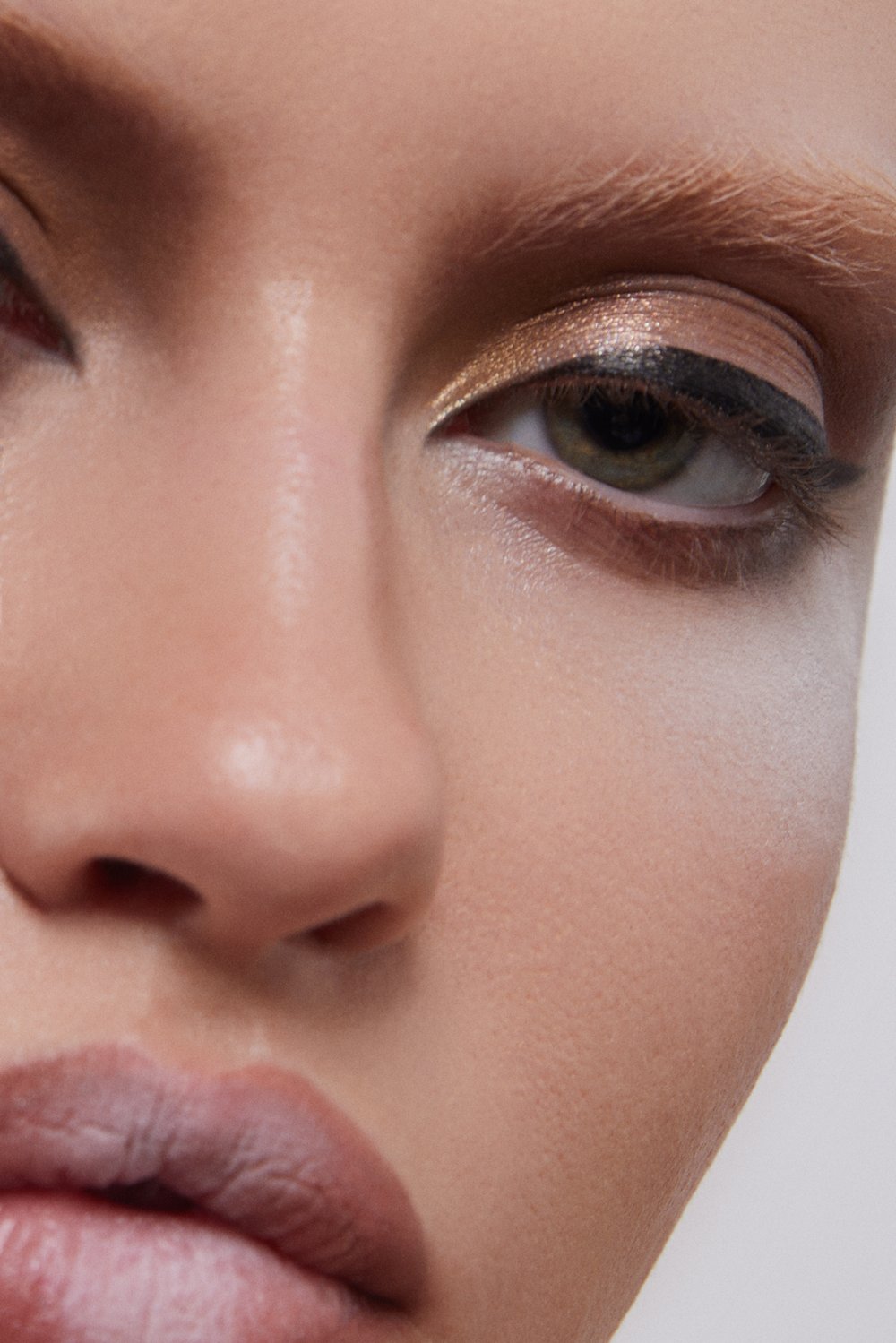 Close-up portrait of a woman with dramatic eye makeup and light eyebrows against a bright background in a beauty editorial shot.