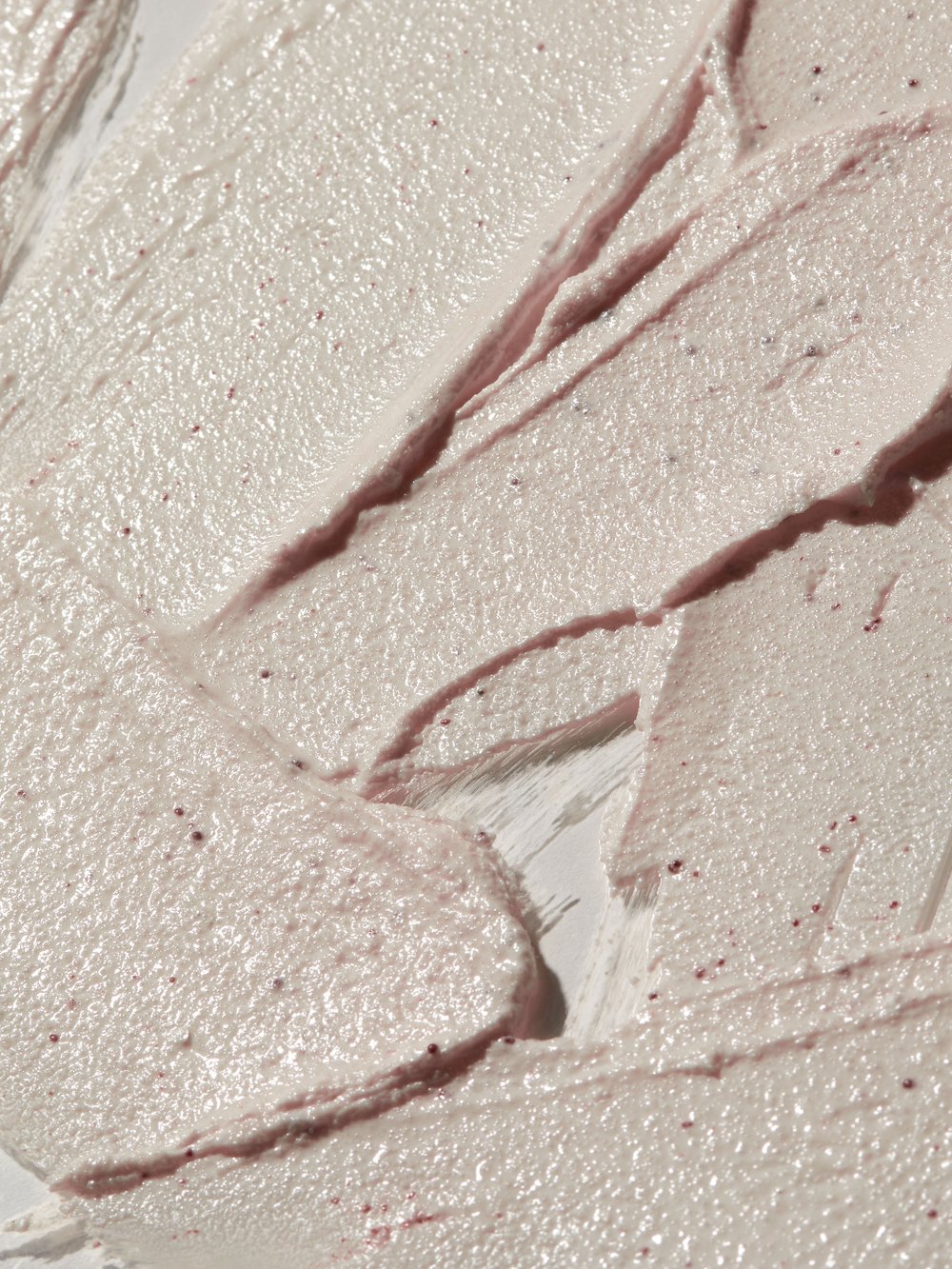 Close-up of cosmetic cream with a thick, spreadable texture, featuring small granules and a light, neutral color palette for skincare.