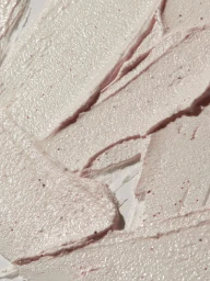Close-up macro shot of textured pink cosmetic cream or scrub swatched on a white surface with small exfoliating particles.