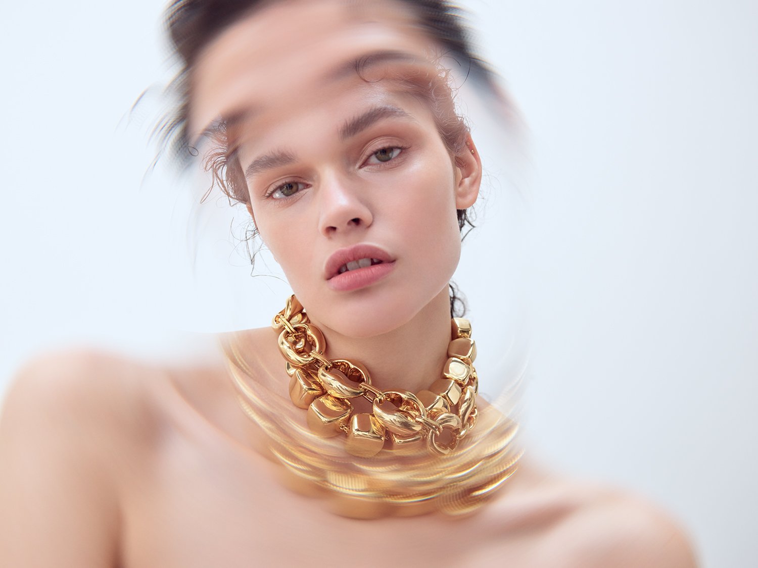 Close-up studio shot of a woman wearing a gold chain necklace, featuring soft lighting and a blurred background. Beauty and fashion.