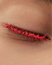 Close-up macro shot of a closed human eye featuring bright red textured eyelashes