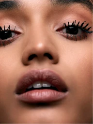 Close-up portrait of a woman showing detailed eye makeup with spiky black mascara and natural lips.