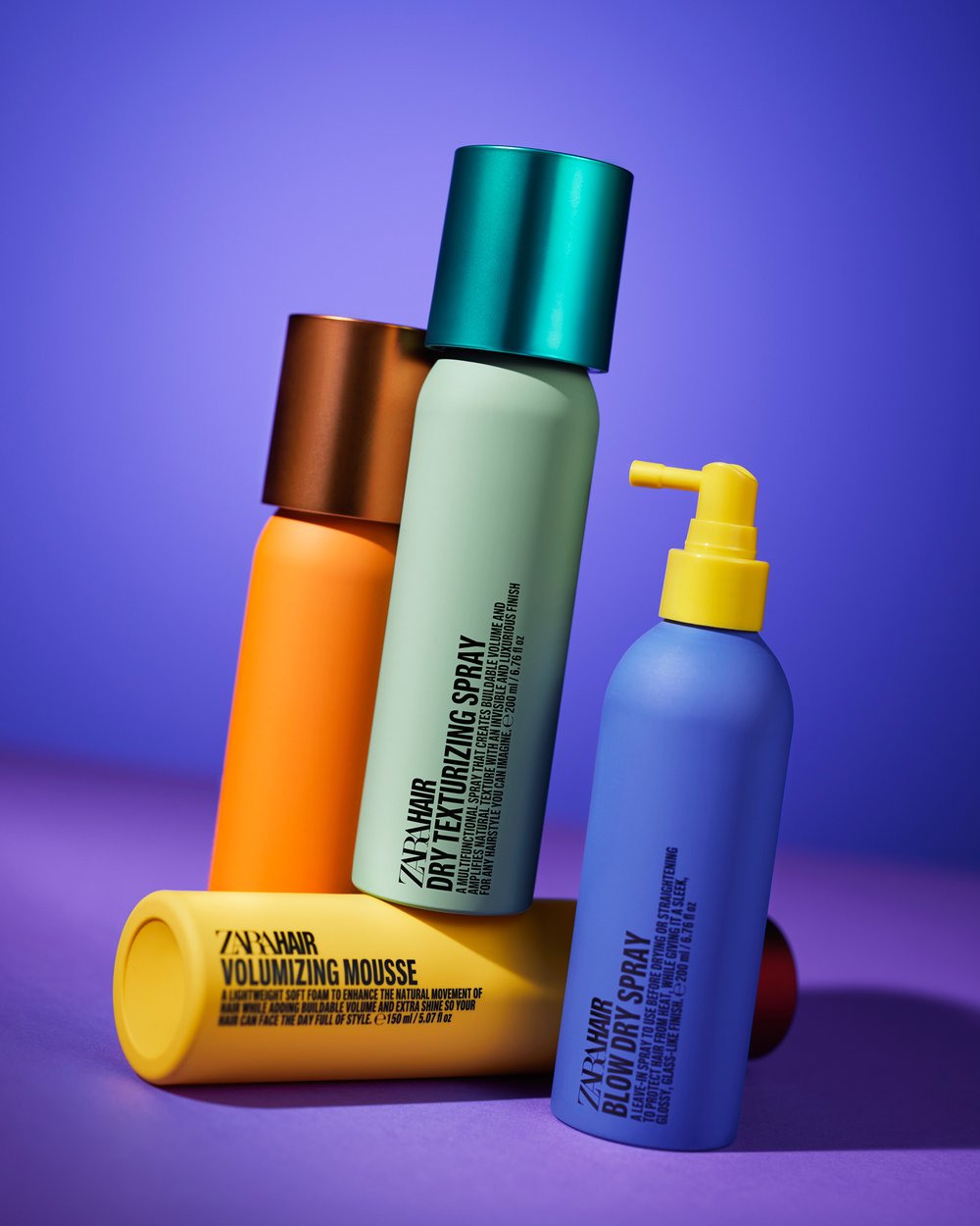 Four colorful ZARA hair products on a purple surface with orange, blue, green, and yellow bottles in a studio setting.