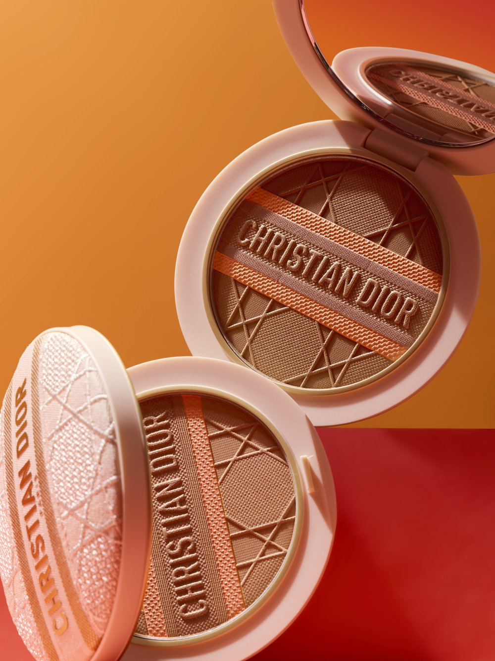 Close-up studio shot of two Dior Forever Couture Perfect Cushion compacts, stacked on a two-tone orange and red background.