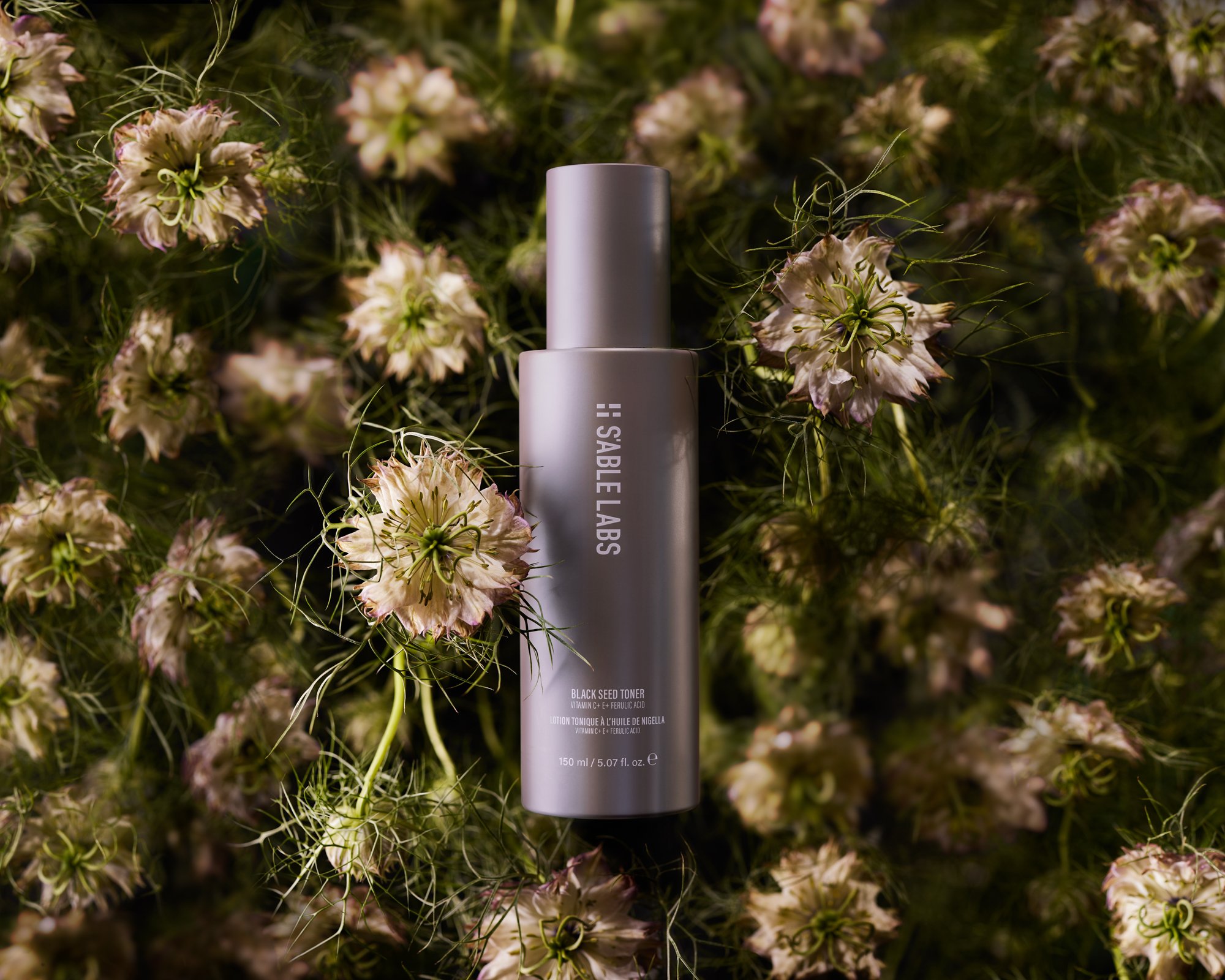 Studio shot of Sable Labs toner bottle on a bed of dark green stems and unique blossoms with cream-colored petals and green centers.