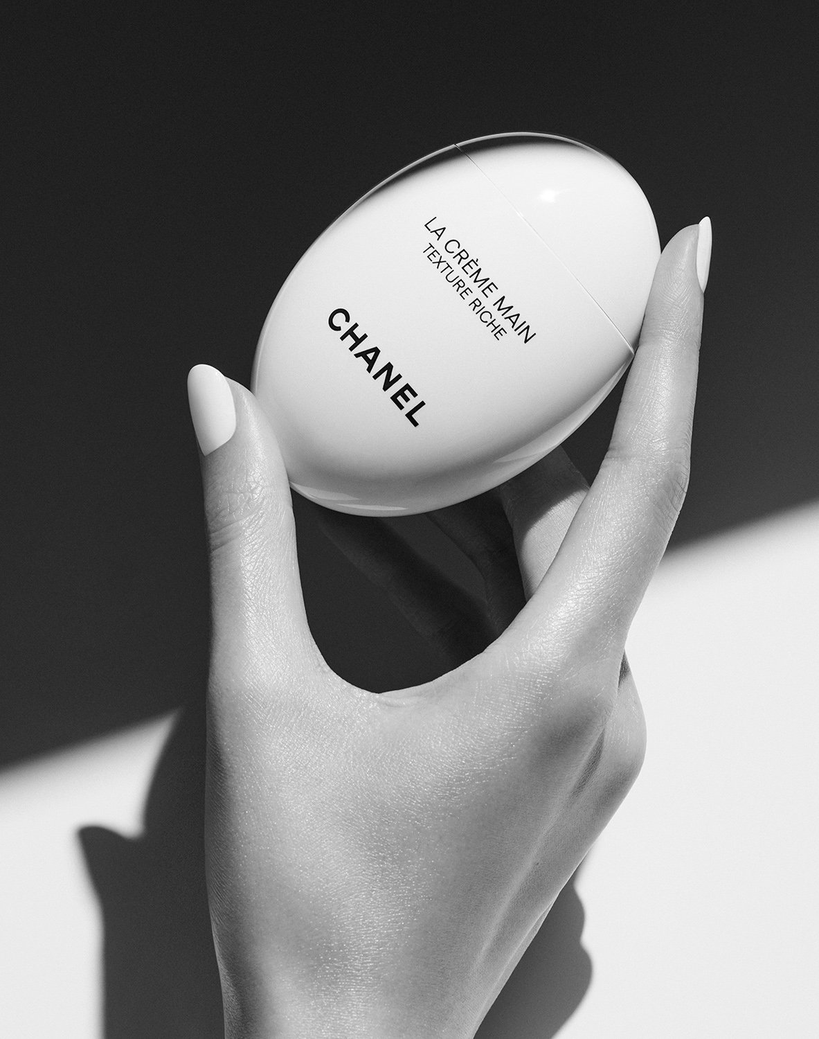 Hand holding Chanel La Crème Main Texture Riche cream with black and white tone and a shadow background for beauty.