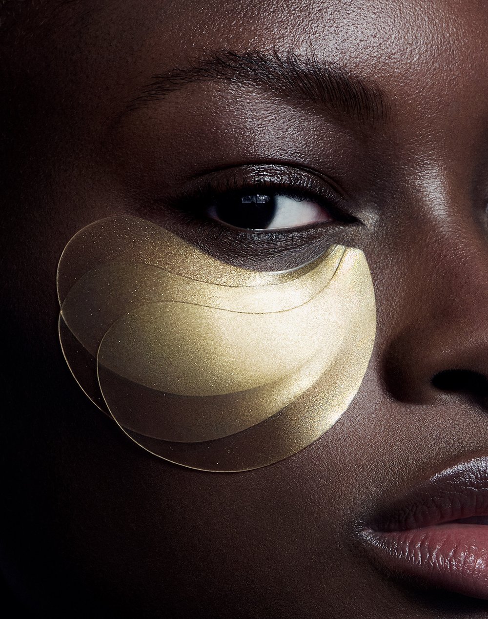 Close-up of an African American woman wearing gold eye patches. Beauty shot focuses on skincare, and eye treatment for anti-aging benefits.