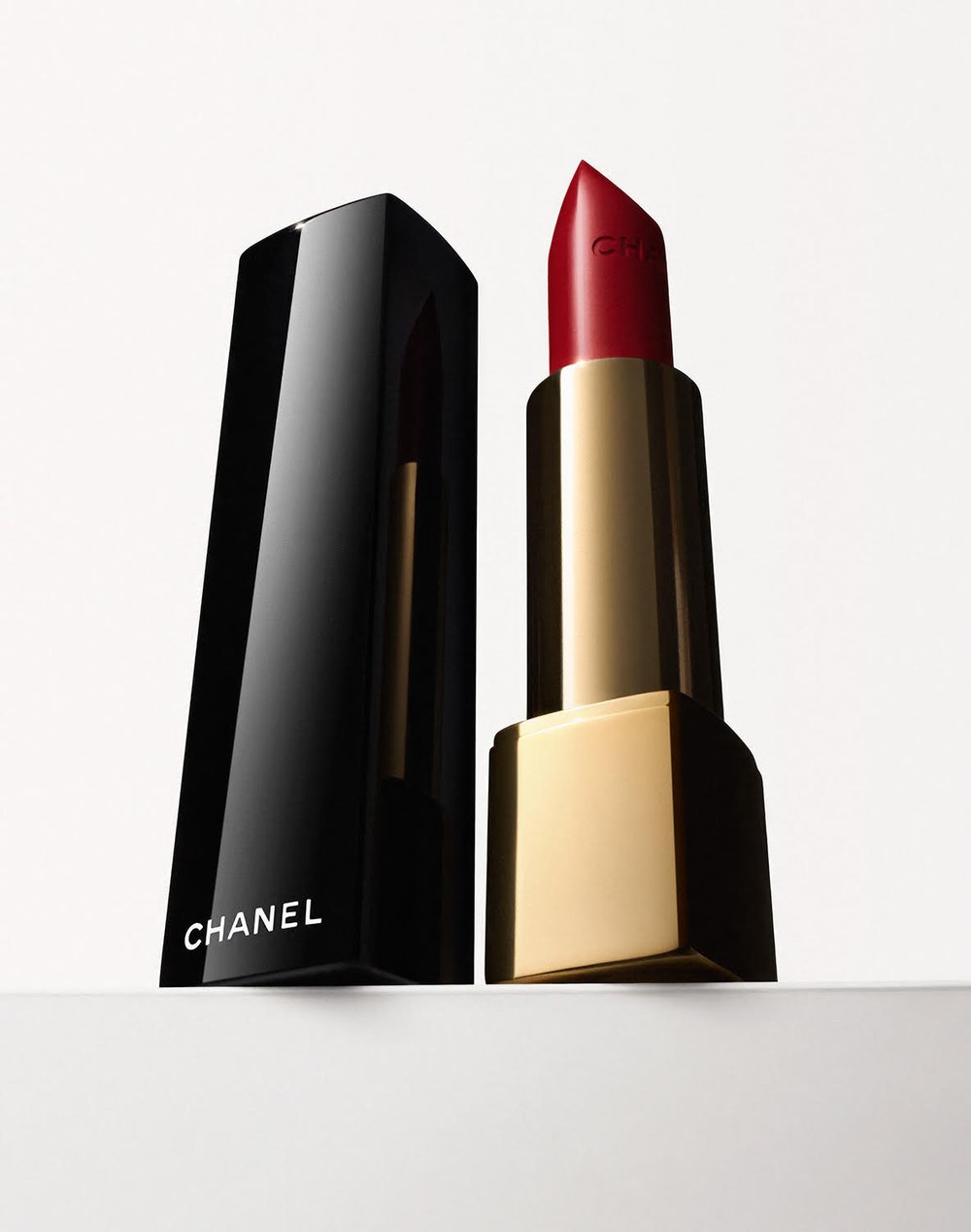 Close-up studio shot of red Chanel lipstick with its black and gold case and cap, isolated on a white surface.