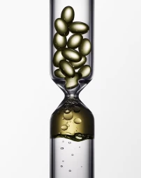 Close-up of golden capsule pills falling through a clear glass hourglass container against a white background.