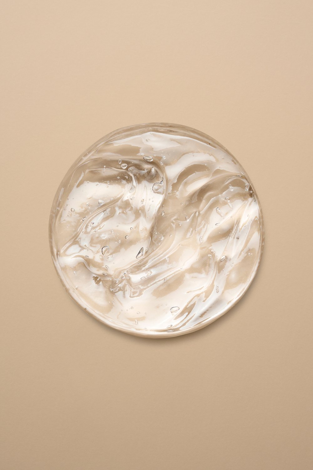 Clear, thick cosmetic gel on a beige backdrop. The gel has a viscous texture and contains tiny air bubbles, illuminated by bright light.