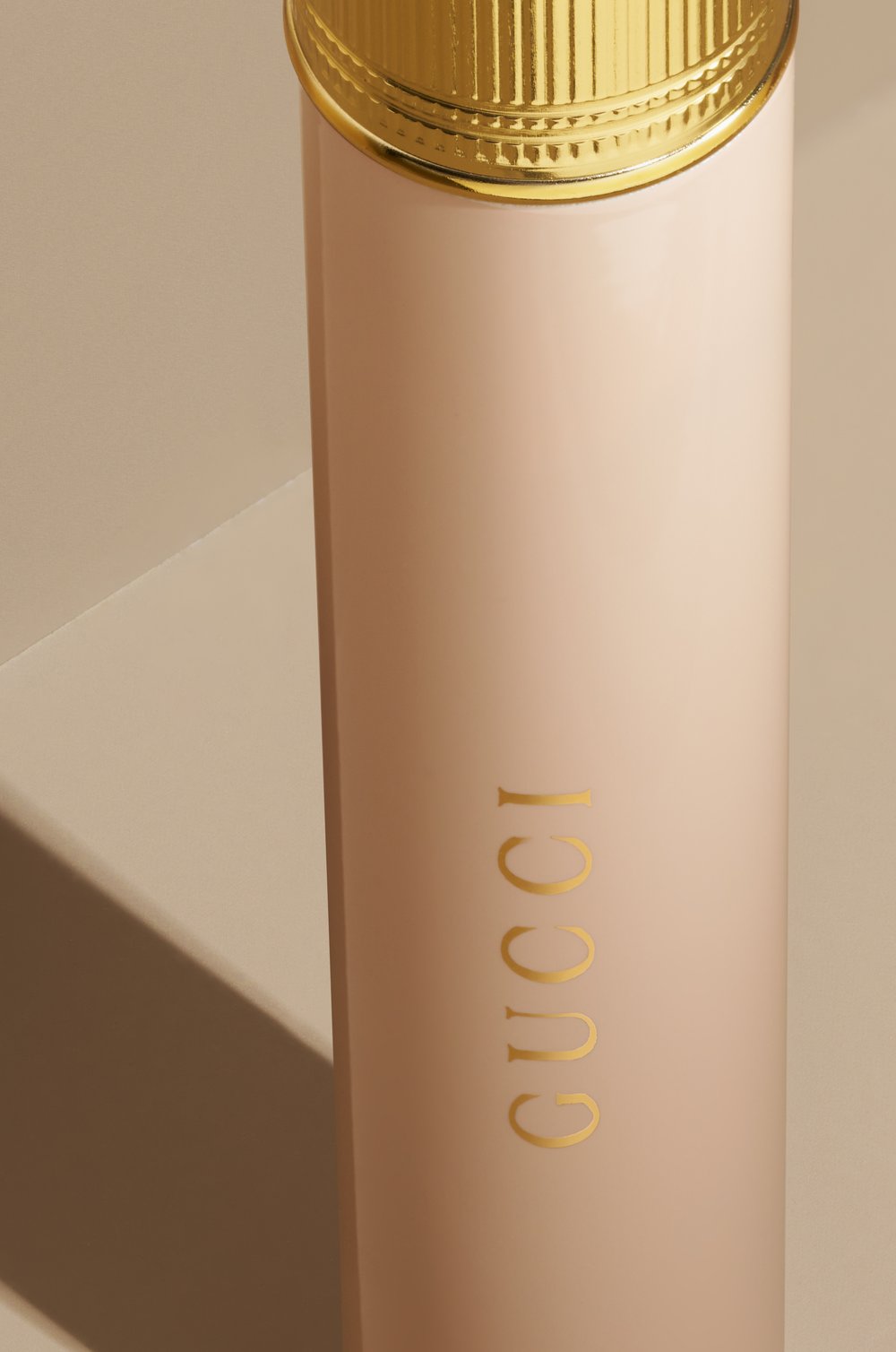 Close-up of a pink Gucci perfume bottle with a golden cap, showcasing the brand logo against a neutral background.