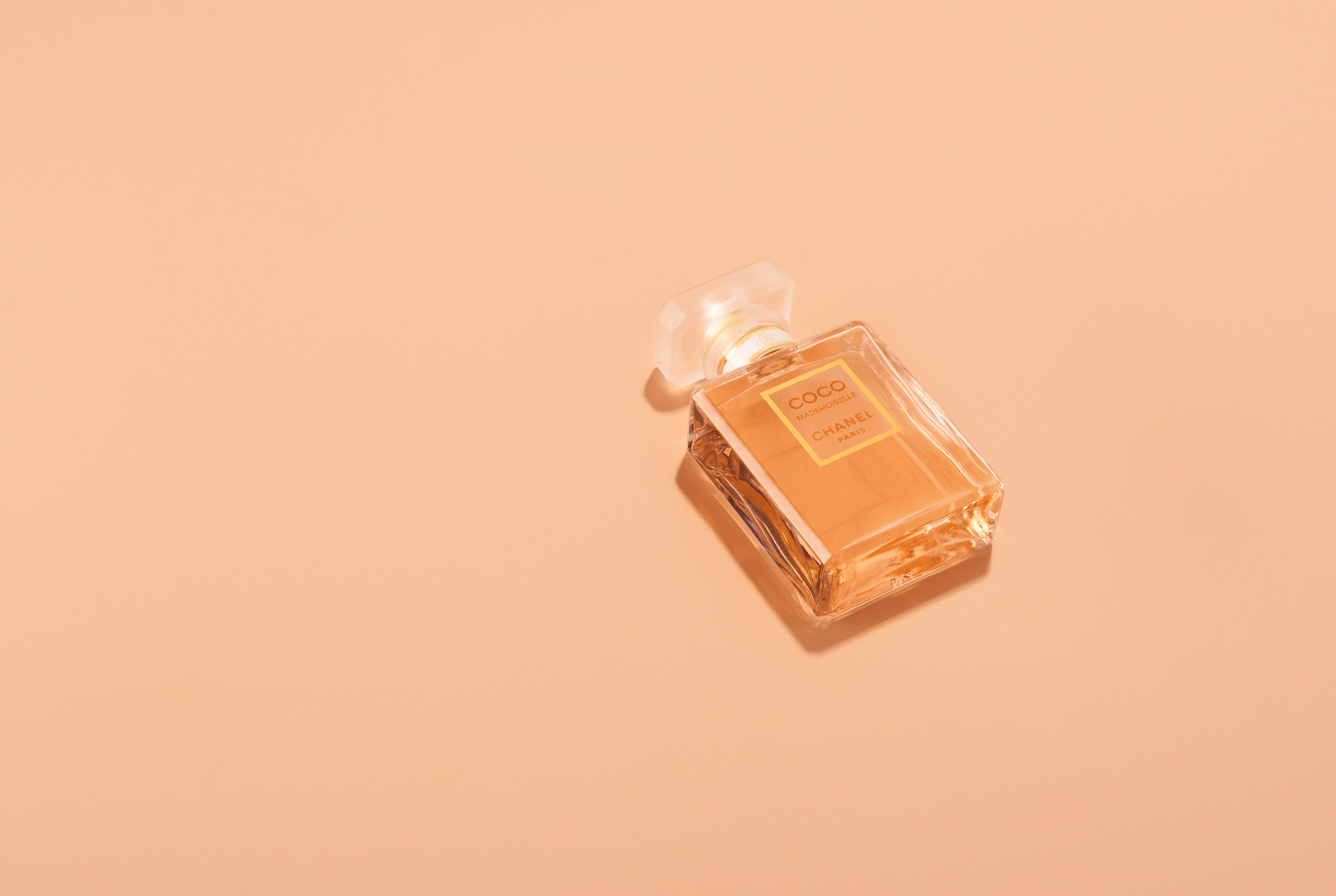 Close-up of a 'Coco Mademoiselle Chanel Paris' perfume bottle against a peach background, showcasing beauty and elegance in simple studio shot.