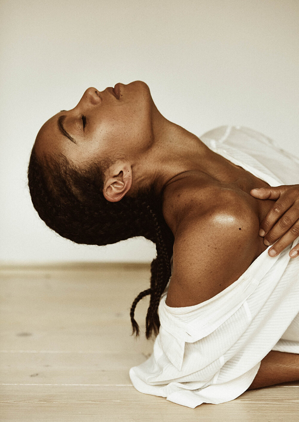 Portrait of a Black woman reclining with closed eyes in a white shirt. She has long dark hair in braids and a relaxed expression.
