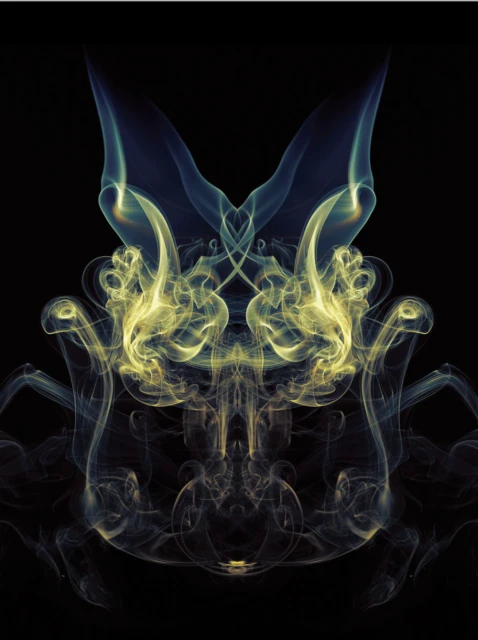 Abstract symmetrical smoke pattern against a black background, featuring delicate wisps of yellow, blue, and white smoke creating a ghostly figure.
