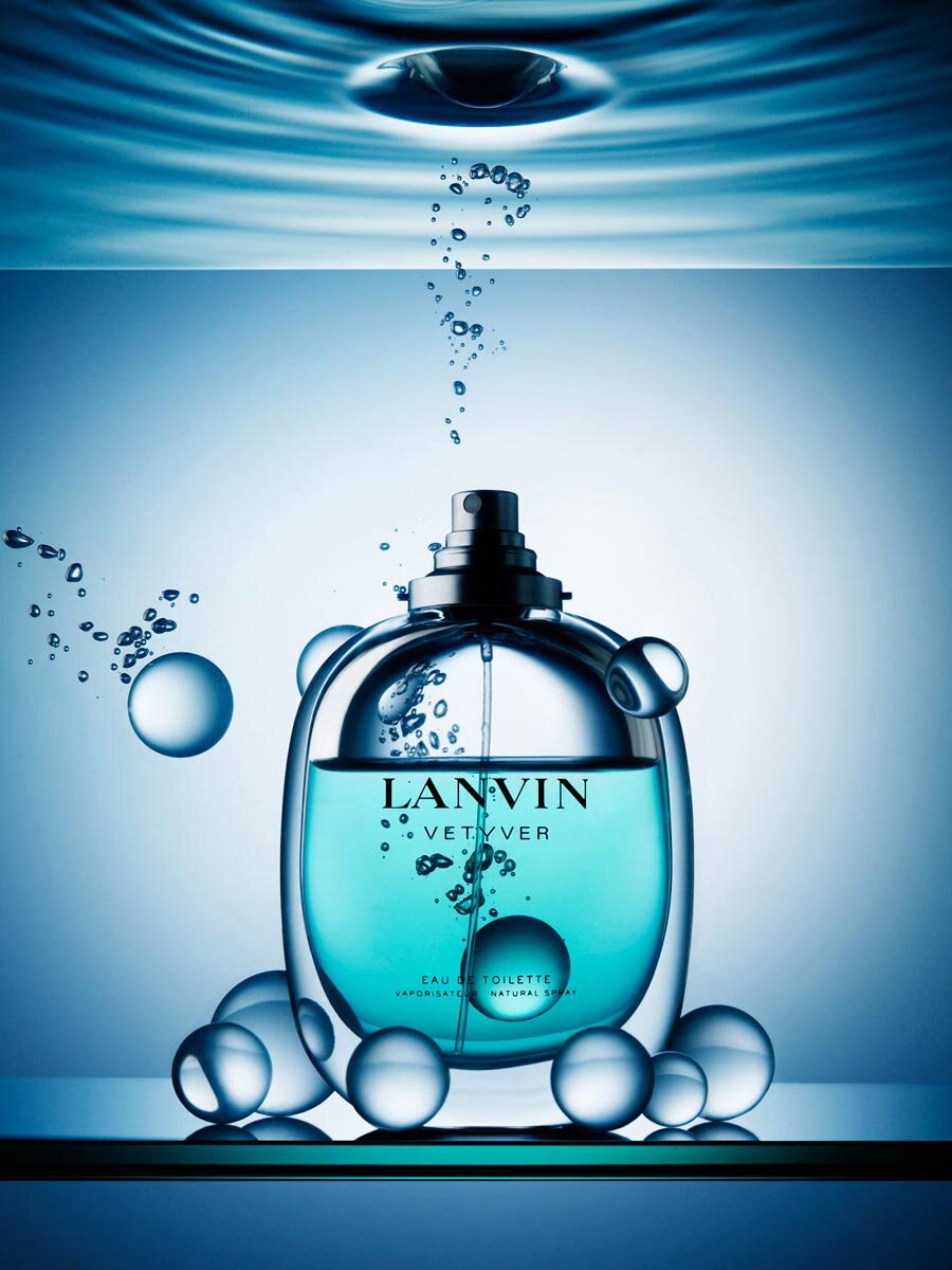 Lanvin Vetyver eau de toilette bottle in blue liquid with bubbles, against a light blue gradient background. Perfume still life.