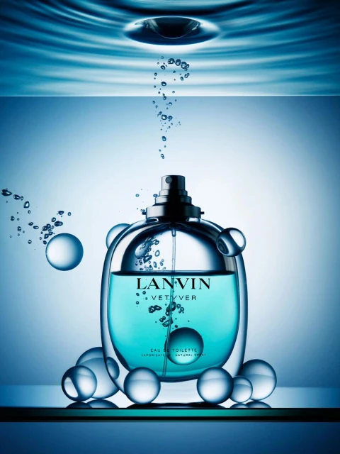 Lanvin Vetyver eau de toilette bottle in blue liquid with bubbles, against a light blue gradient background. Perfume still life.