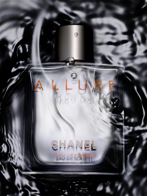 Close-up studio shot of a clear Chanel Allure Homme Eau de Toilette bottle with a silver cap, surrounded by water, and sleek dark background.