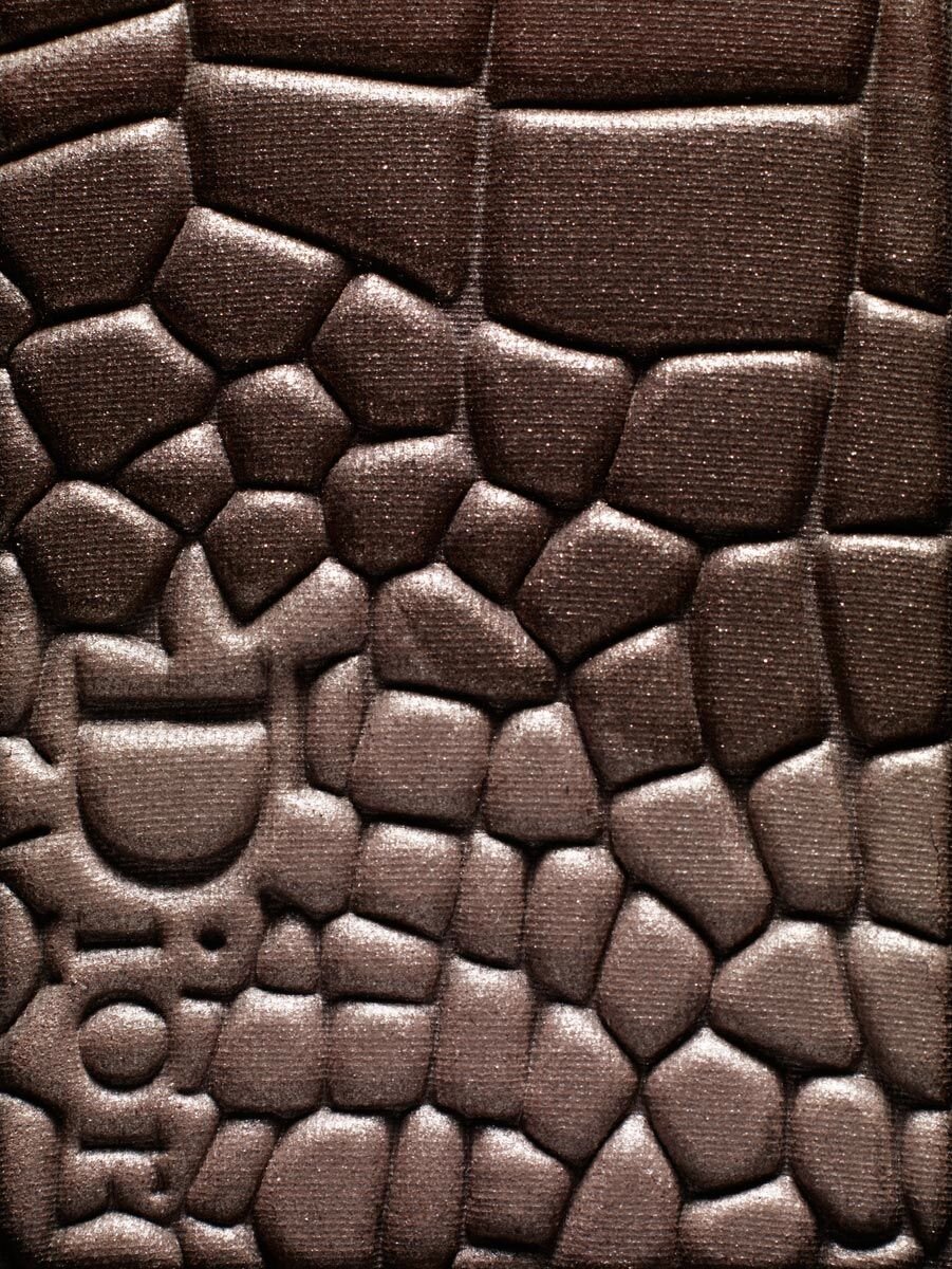 Close-up of brown eyeshadow with textured, embossed pattern and a designer logo for beauty or cosmetics advertising or social media content.