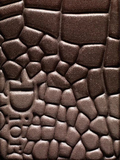 Close-up of brown eyeshadow with textured, embossed pattern and a designer logo for beauty or cosmetics advertising or social media content.