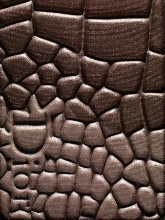 Close-up of brown eyeshadow with textured, embossed pattern and a designer logo for beauty or cosmetics advertising or social media content.