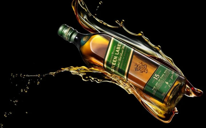 Studio shot of a Johnnie Walker Green Label whisky bottle surrounded by splashes of liquid against a black background, product shot.