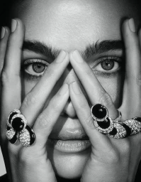 Close-up monochrome portrait of a model holding hands framing her face, showcasing large diamond and black stone rings