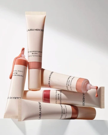 Arrangement of Laura Mercier Tinted Moisturizer Blush tubes in various shades on a white surface, displaying beauty product assortment.