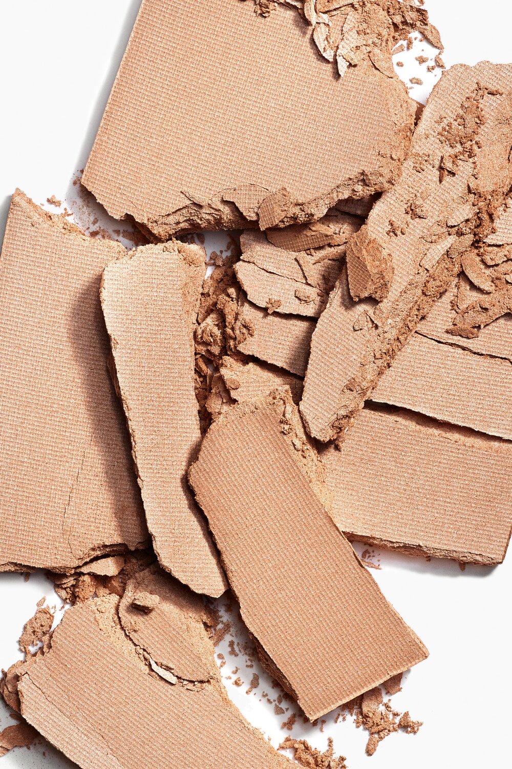 Close-up studio shot of broken beige powder cosmetic product, isolated on white, suitable for beauty, makeup, and skincare themes.