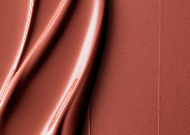 Abstract image of glossy, wave-shaped, terracotta-colored material with smooth textures and bright highlights, capturing a sleek and modern aesthetic.