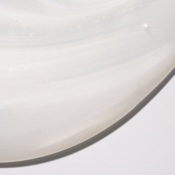 Close-up of a thick, glossy, white liquid with swirls against a plain white background, showcasing texture and light reflection.