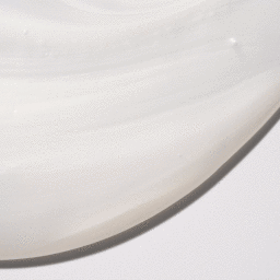 Close-up macro shot of white cosmetic cream smear on a clean pale background with smooth viscous texture