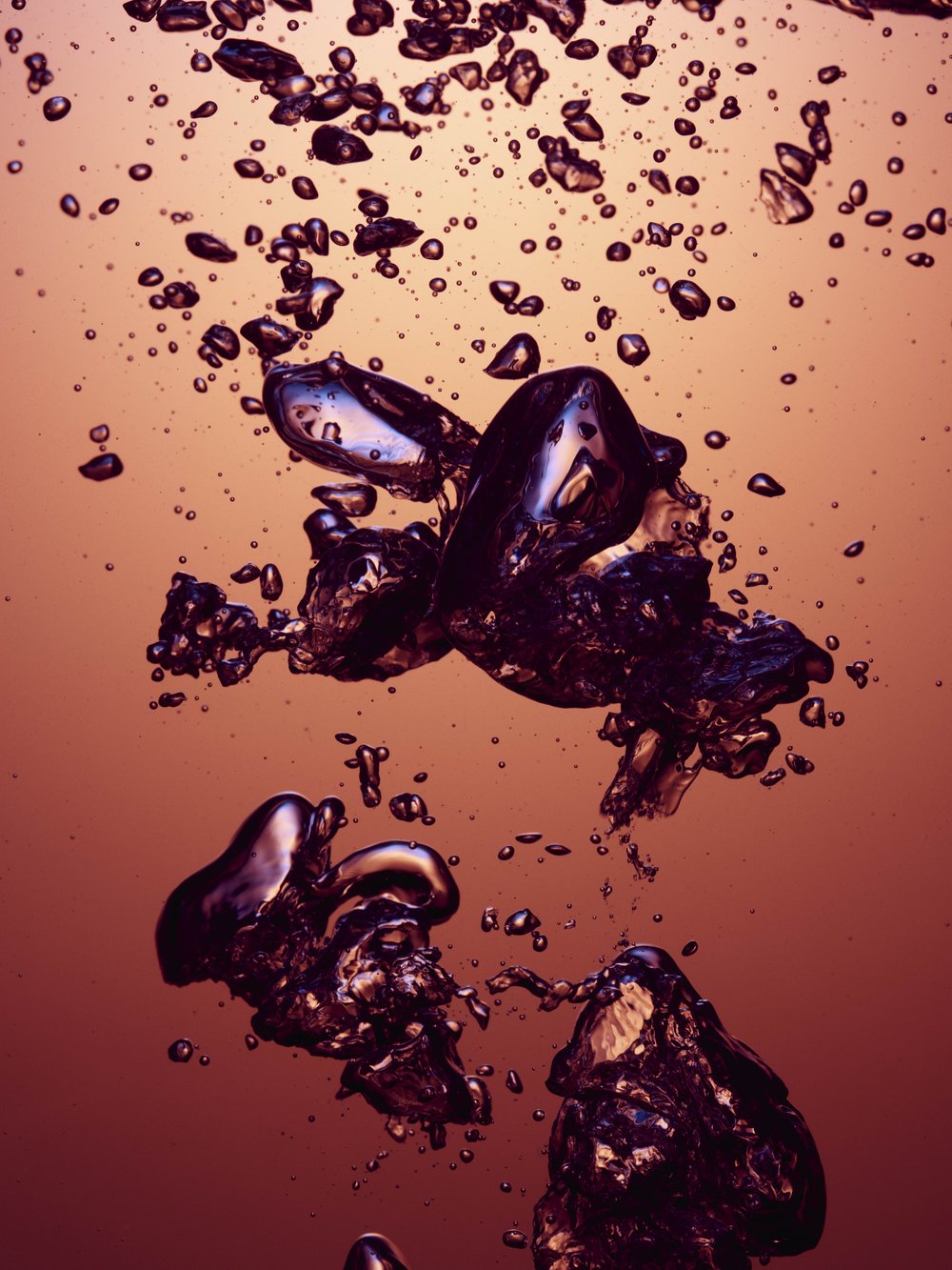 Close-up of bubbles in liquid with purple hue against a coral-colored background, creating an abstract underwater effect.