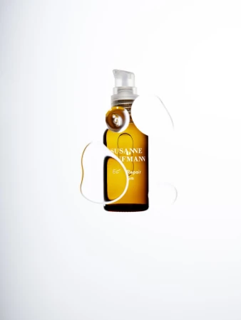 Amber glass bottle of Susanne Kaufmann hair repair serum with pump dispenser on a white background with simulated liquid drops.