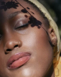 Close-up portrait of a Black woman with closed eyes and leaf shadows cast across her face by Simrah Farrukh.