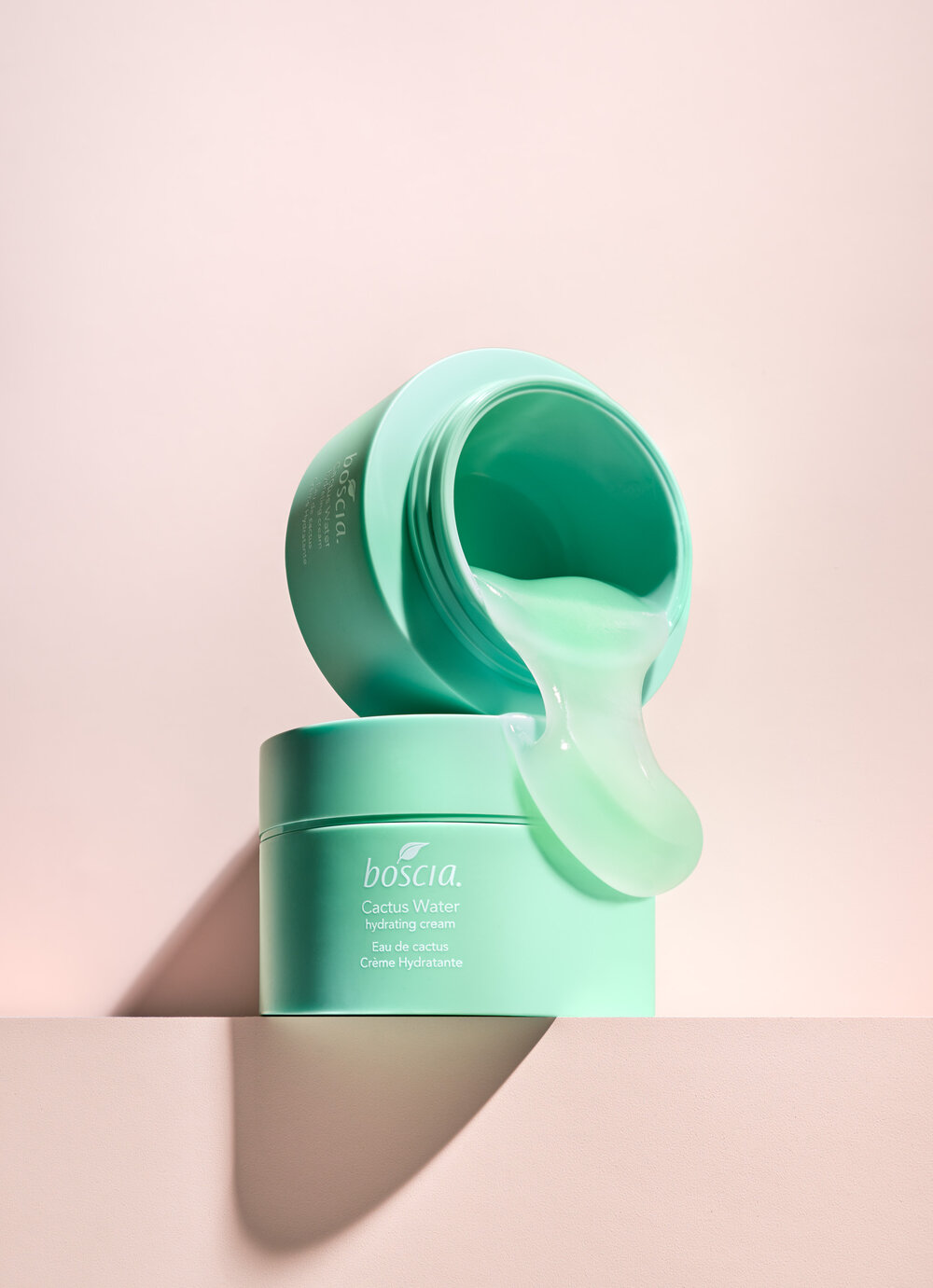 Boscia Cactus Water Hydrating Cream product shot. Teal jar with clear gel pouring out, stacked against a soft pink background.