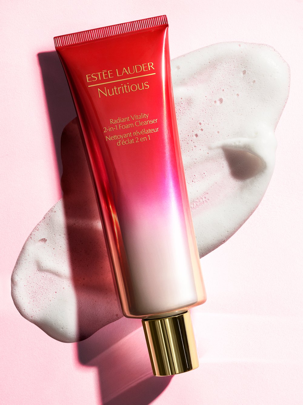 Estee Lauder Nutritious Radiant Vitality 2-in-1 Foam Cleanser tube on a pink surface with a streak of cleansing foam alongside it.