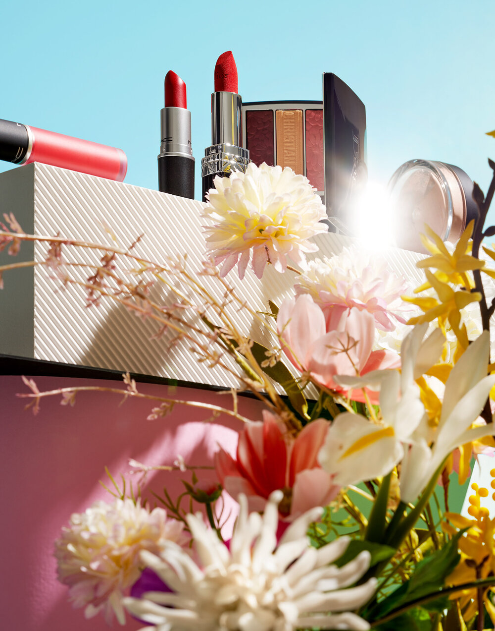 Cosmetics and flowers arranged on a striped box against a blue background in a product photography studio setting, capturing beauty and color.
