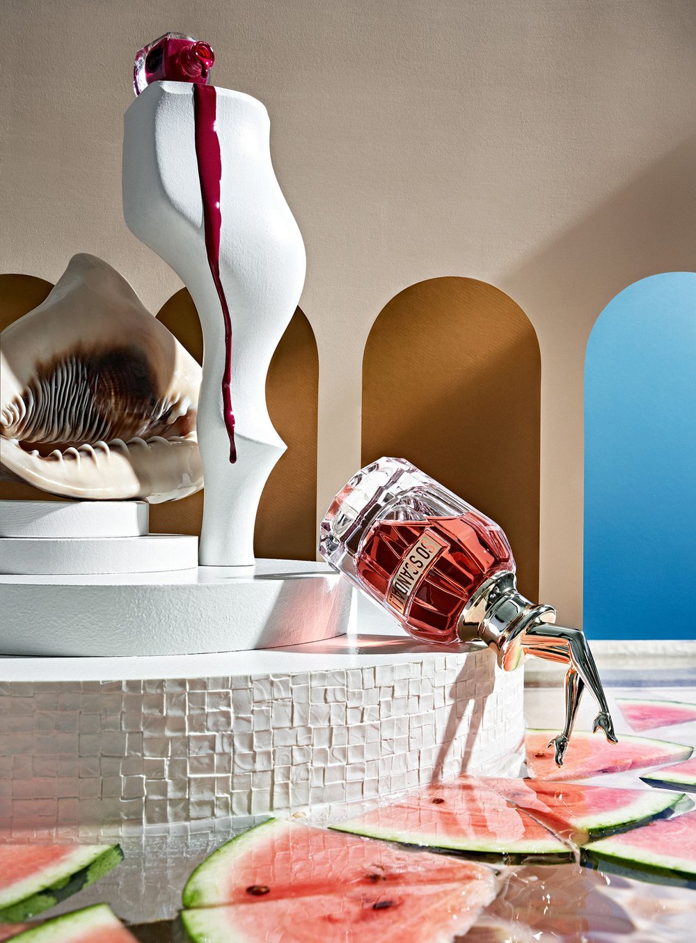 Glamorous perfume bottle with leg-shaped stand on a patterned platform next to a white mannequin torso and watermelon slices.