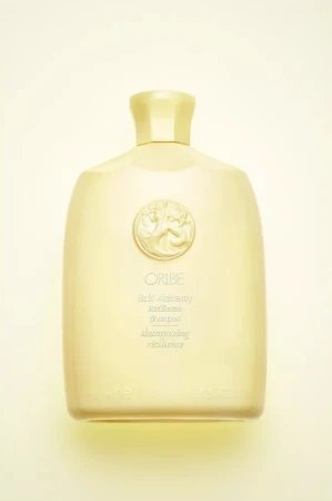 Oribe Gold Lust Nourishing Hair Oil bottle on a light yellow background. The bottle has a gold cap and a circular emblem.