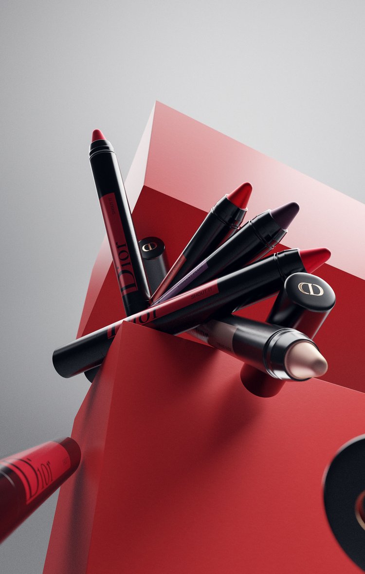 Eye makeup pencils from Dior in red and black on a red geometric surface against a grey background in a studio product shot.