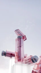 Floating pink cosmetic lip balm packaging tubes arranged vertically against a pale sky background