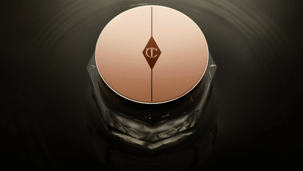 Cosmetic cream jar with a rose-gold lid and clear container sitting on a dark surface and reflecting light, beauty product.