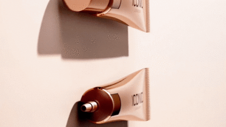 Two metallic rose gold cosmetic tubes mounted on a light background with dramatic cast shadows.