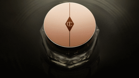 Top down view of a cosmetic jar with a rose gold circular lid featuring a central diamond logo, set on dark rippling water.