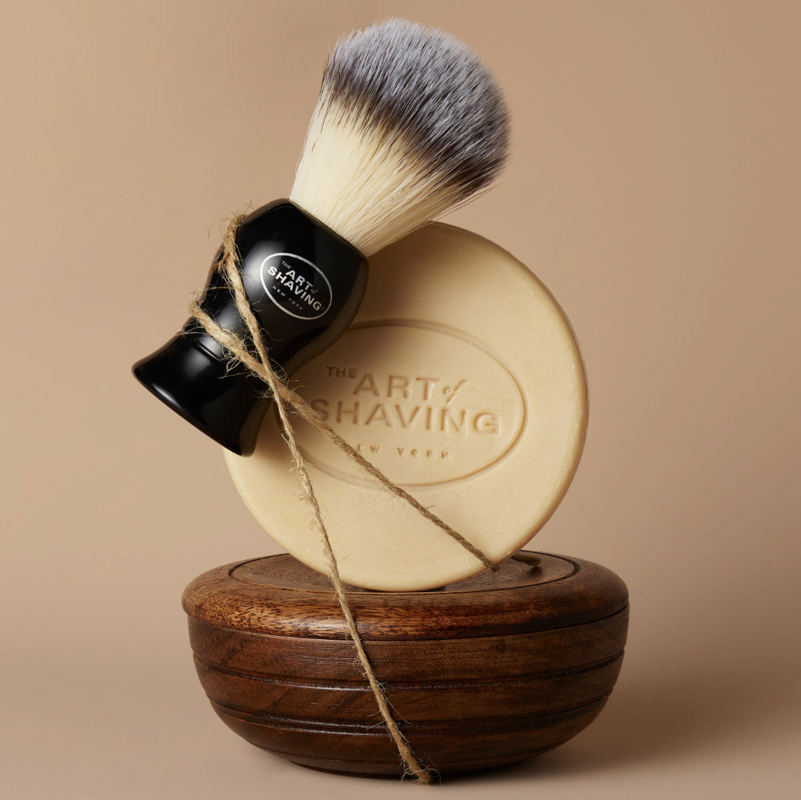 Elevated view of shaving brush, soap, and wooden bowl in a studio setting, showcasing grooming and self-care products against a neutral backdrop.