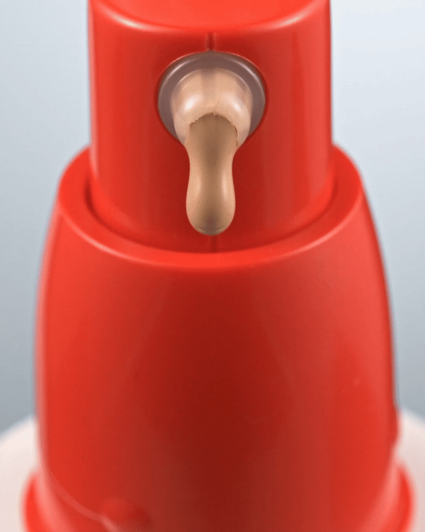 Close-up of a red and white bottle with a drop of beige liquid emerging from the dispenser. The bottle is set against a blue background.
