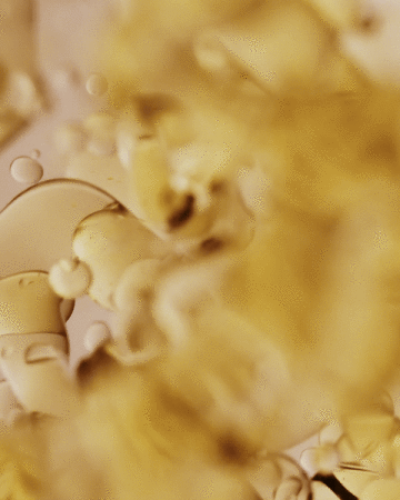 Abstract close-up of golden viscous liquid with droplets, light and shadows play across the oily surface, creating a textural effect.