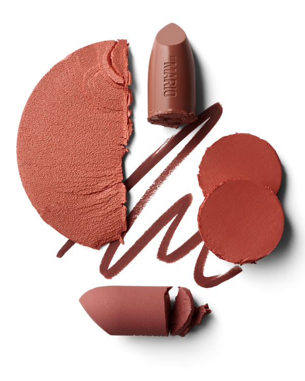 Still life flat lay of lipstick, makeup powder, and eyeliner in shades of brown and peach on a black background for beauty content.