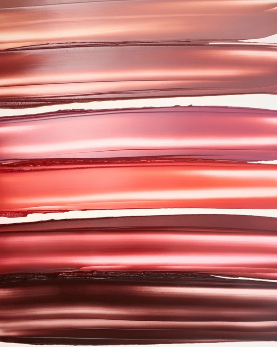 Horizontal cosmetic swatches in various shades of brown, pink, and red showing glossy and matte textures against a light background.