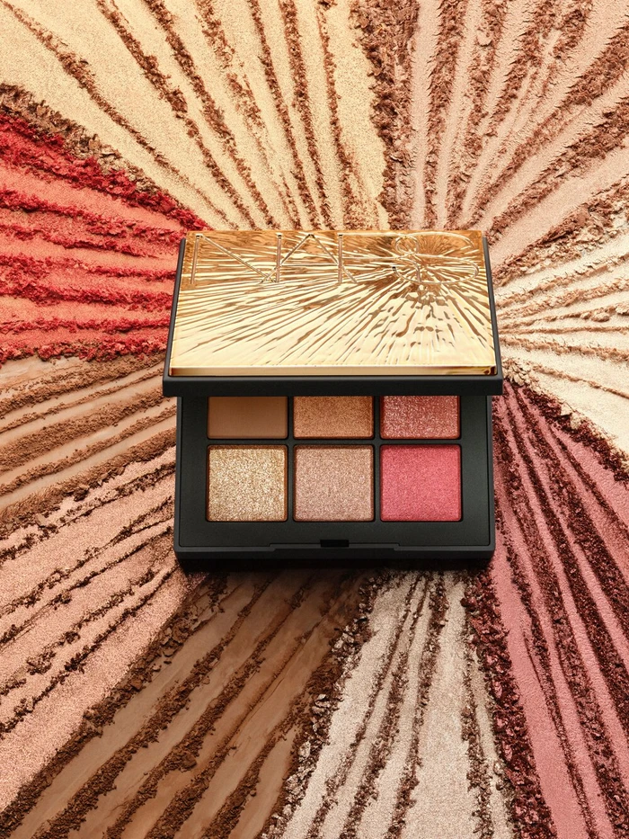 NARS eyeshadow palette with gold lid centered over radiating streaks of colored cosmetic powder